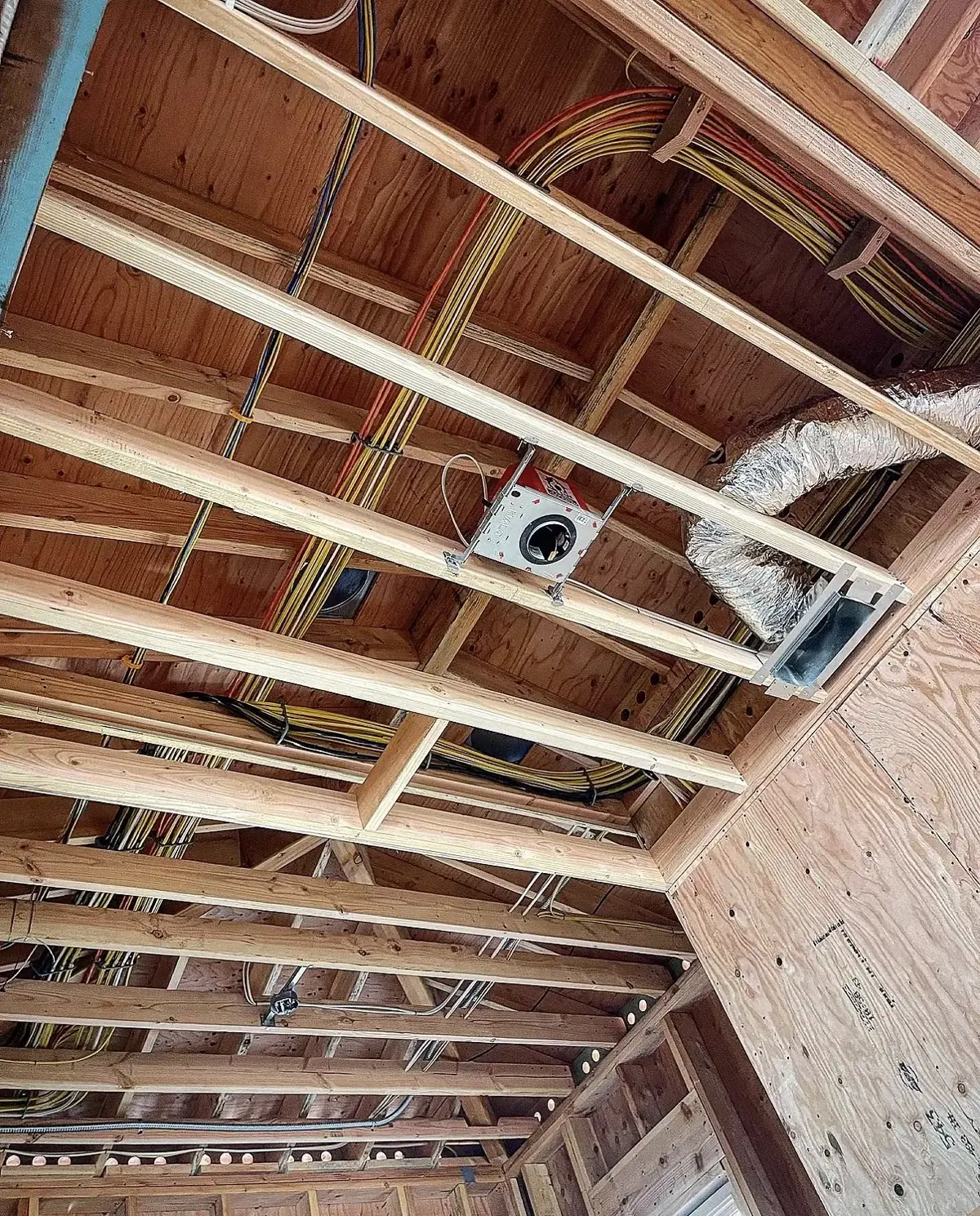 Open ceiling joists with electrical cables run along the framing to an octagon box, flexible duct nearby