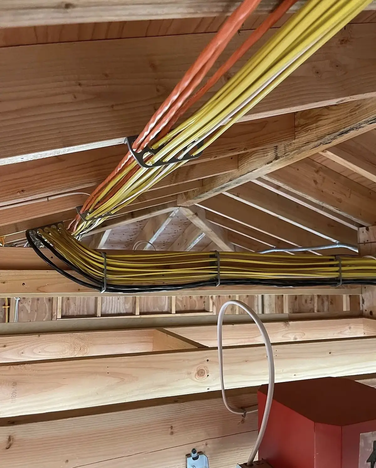 Bundle of yellow electrical cables stapled along wooden roof trusses