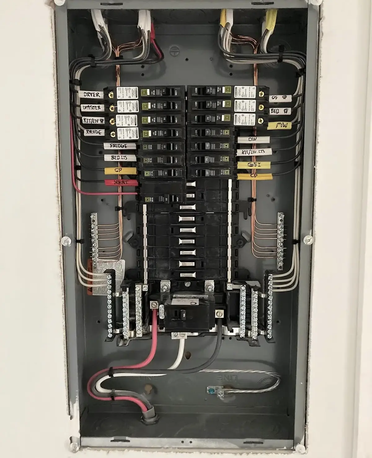 Open residential breaker panel with handwritten circuit labels beside each breaker and conductors dressed to each side
