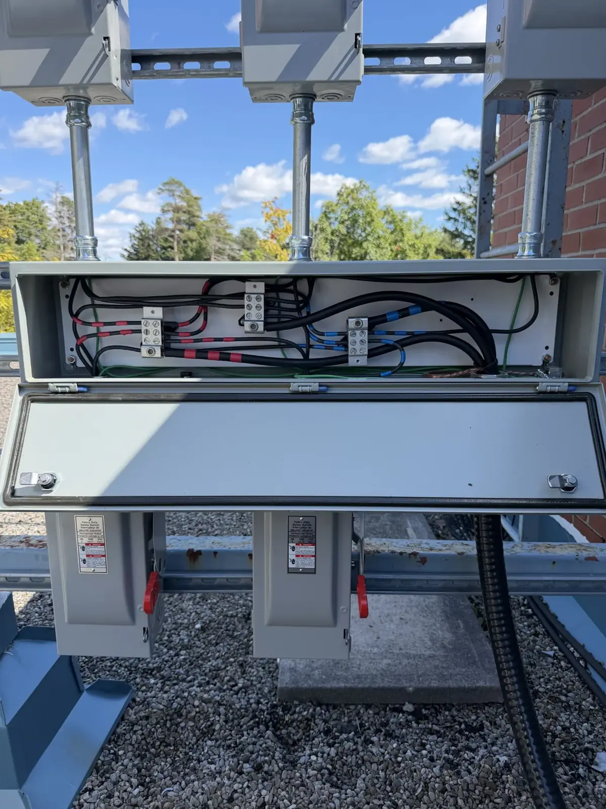 Open rooftop wireway with black conductors routed between disconnect switches
