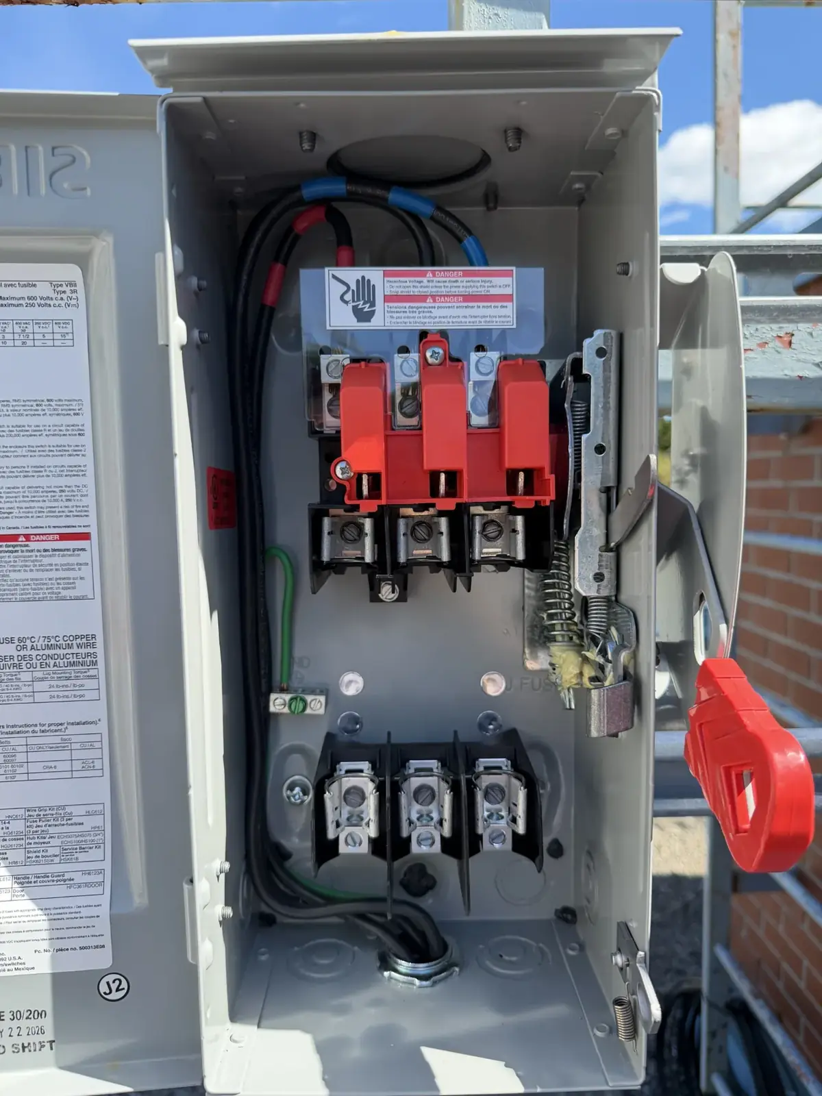 Inside a disconnect switch enclosure: red handle mechanism, line and load terminals and the wiring label