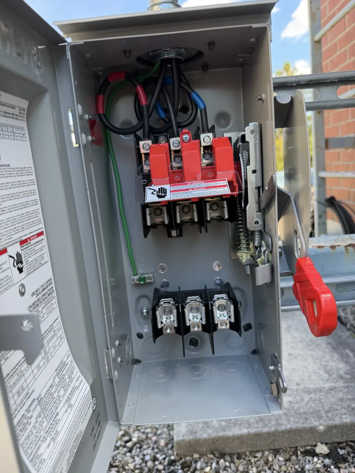 Close view of conductors terminated inside a disconnect switch, with the red operating handle on the right