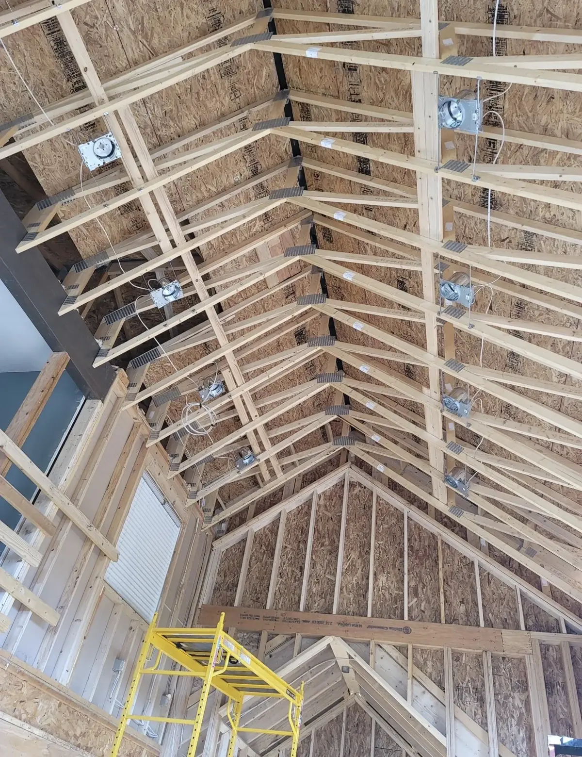 Cathedral ceiling trusses with recessed light housings mounted between them and a scaffold below