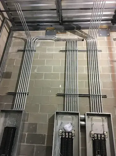 Parallel EMT conduit runs on a concrete block wall, bending overhead into two panel enclosures below