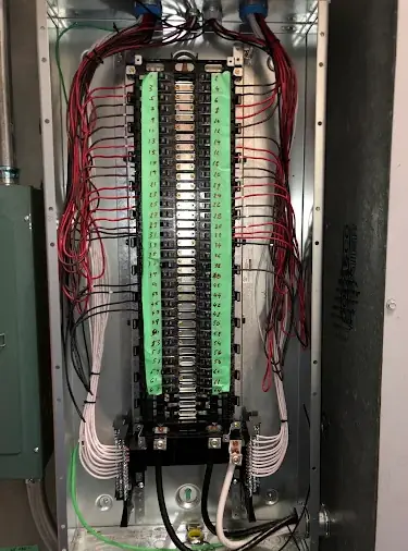 Interior of a large breaker panel with two full columns of breakers, green circuit labels and red and white conductors dressed to the sides