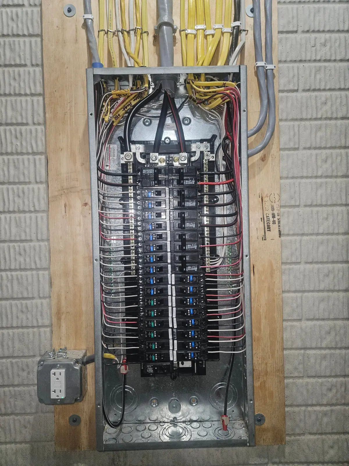 Large residential breaker panel with the cover off, labelled cables entering from the top and conductors dressed neatly to both sides, a GFCI receptacle mounted beside it