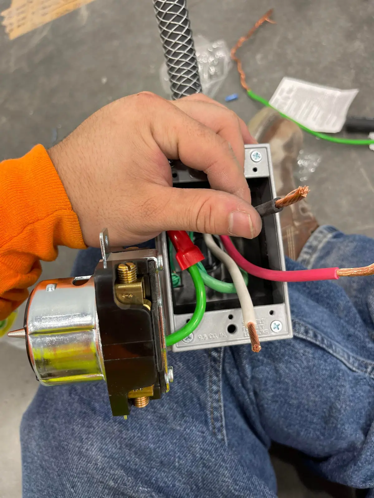 Hand holding a receptacle being wired to stranded red, white and green conductors in a metal box